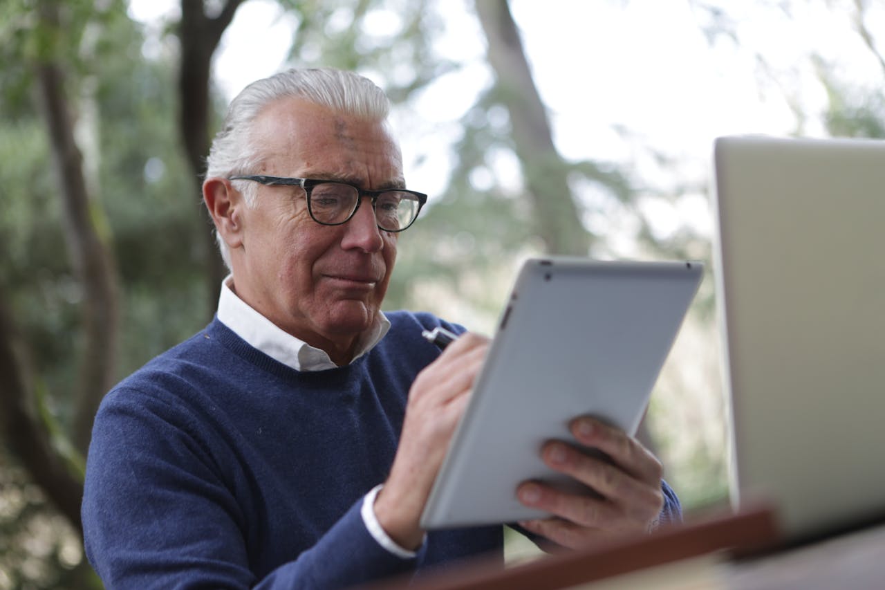 Man in Blue Sweater Holding White Tablet Computer